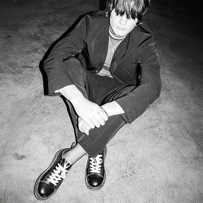 Person wearing a dark suit and black Monkey Boot )MNKY SHOE) sitting on a textured floor.