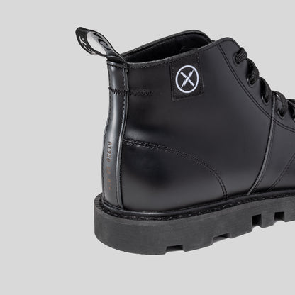 Close-up of the MNKY boot heel showing FACT. logo patch, woven heel pull tab, and welted construction on a gray background.